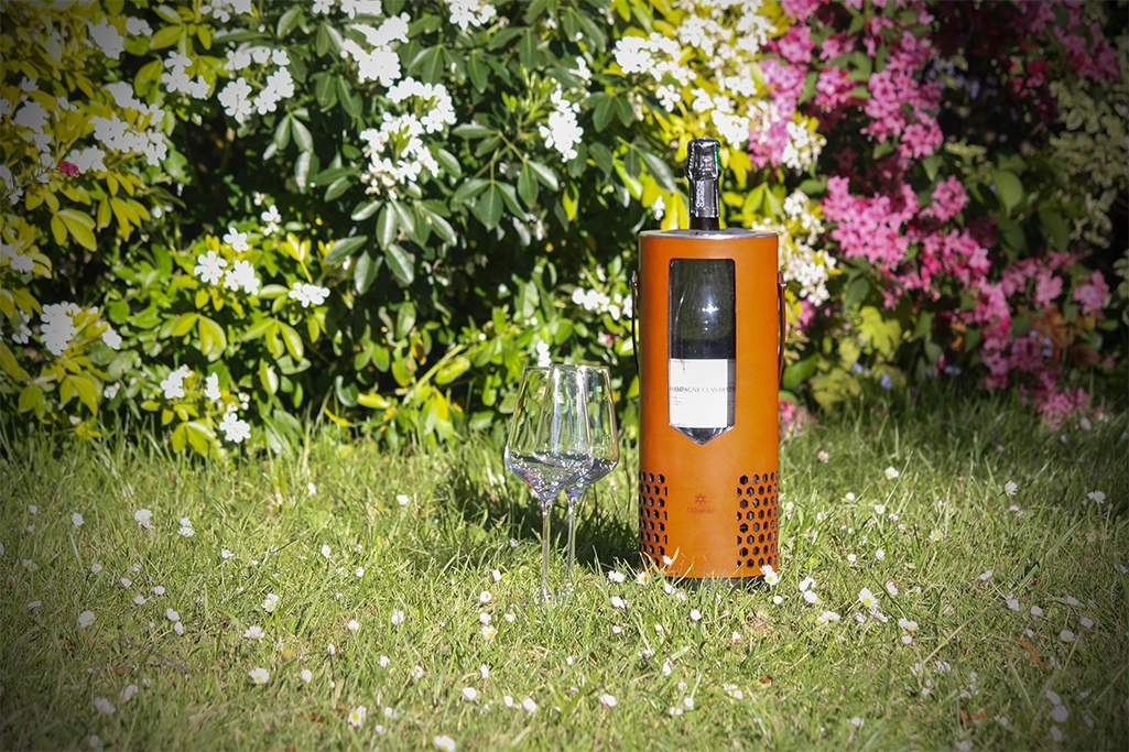 L'Alvéole avec une bouteille de champagne et deux verres de vin dans un jardin.